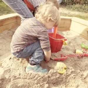 Kind spielt im Sandkasten mit Dach